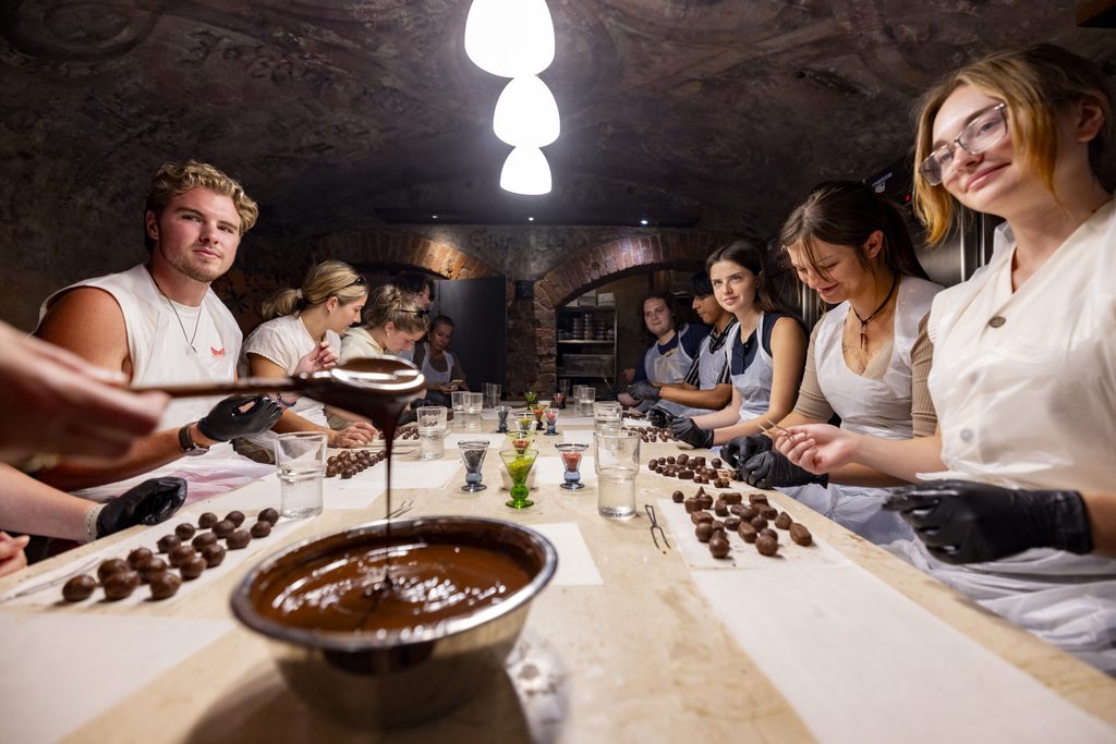 Students in plastic aprons and black latex gloves roll truffles in a brightly lit brick cellar.